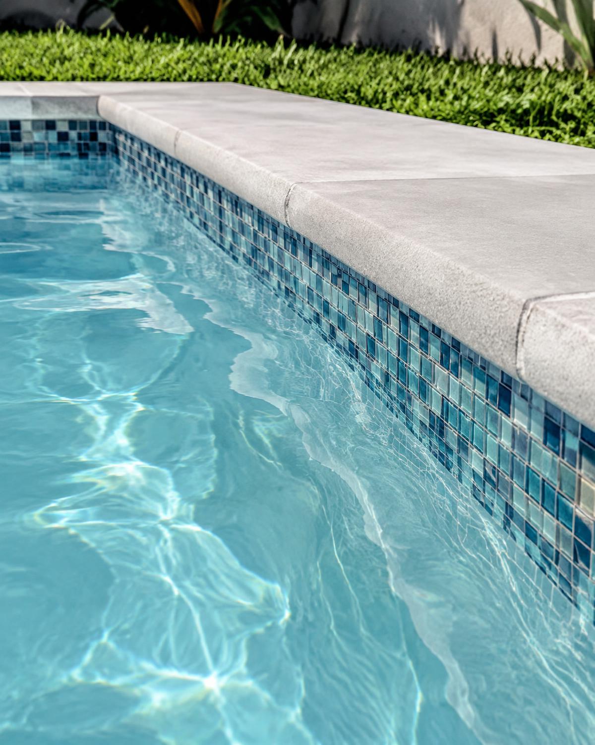 Pool edge with blue glass mosaic tile and light gray coping